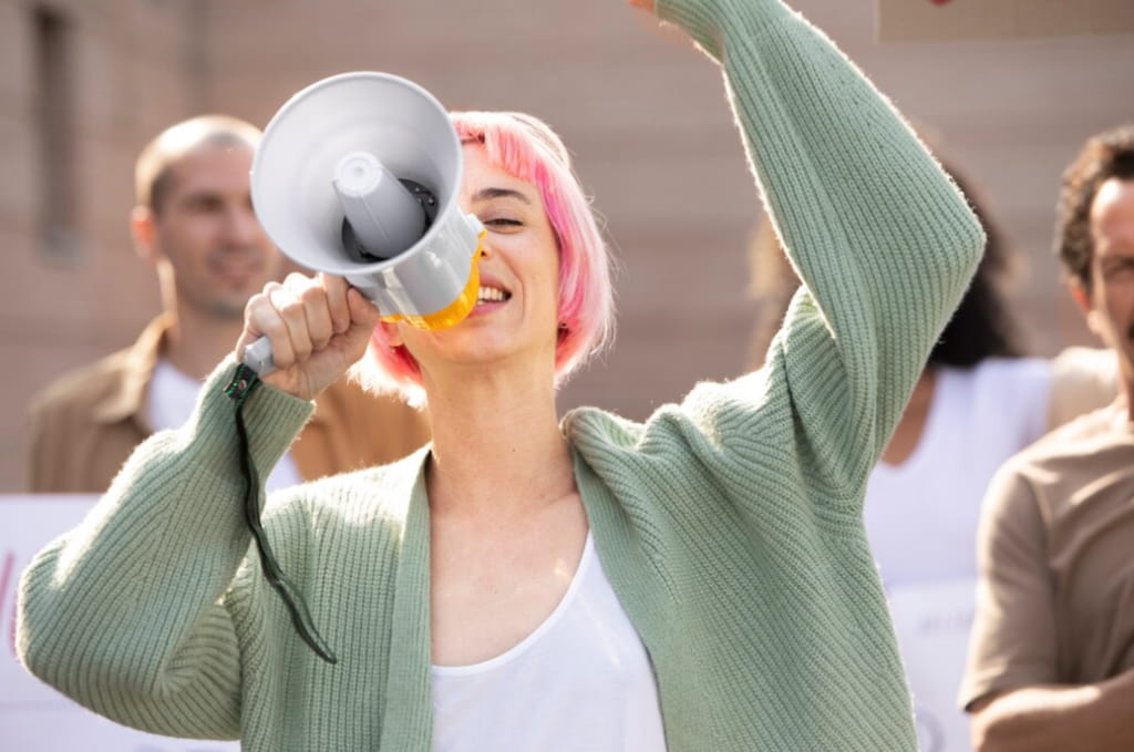 Woman with pink hair speaking into a megaphone at a rally