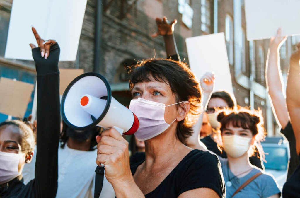 Masked woman speaking through a bullhorn at a rally with other protesters around her