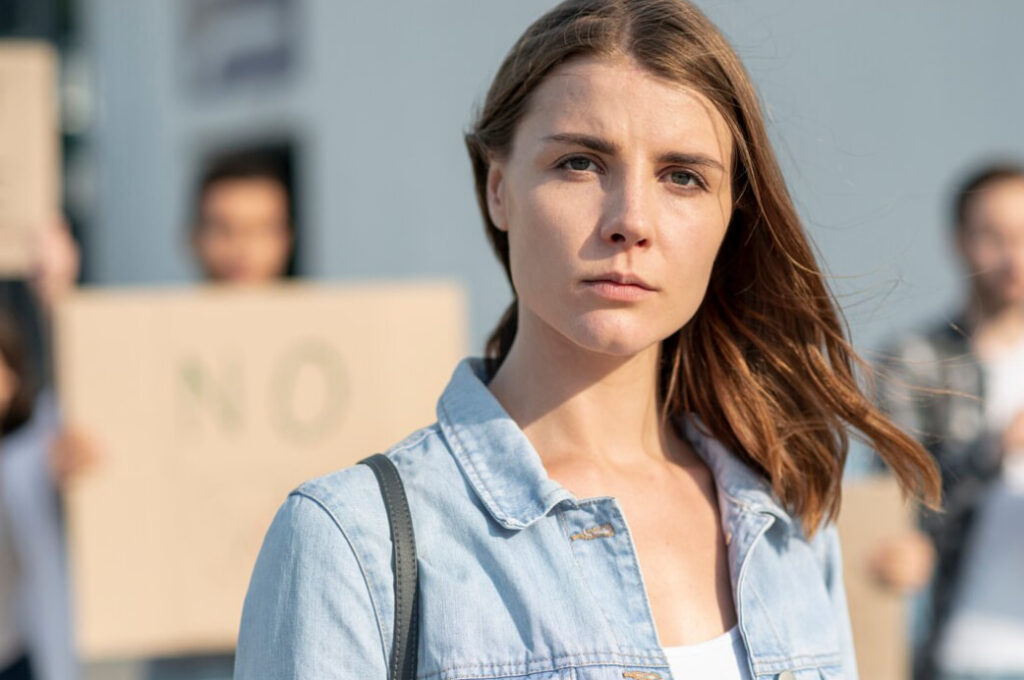 woman in a jeans jacket standing outside, the woman with paper tables behind